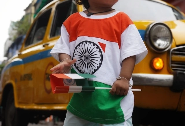 Child proudly wears the Indian national flag and raises the flag of India during a festive celebration.