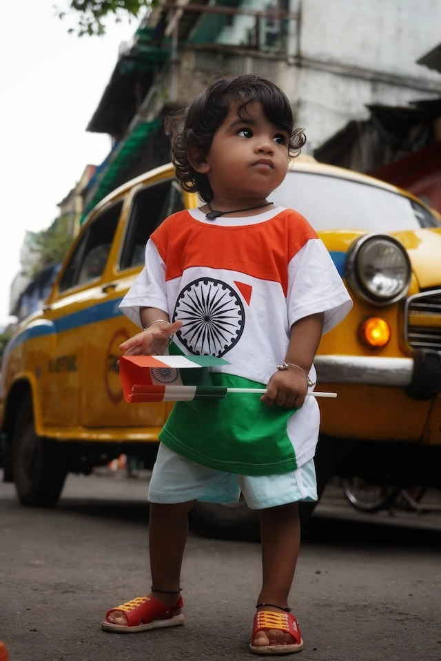 Child proudly wears the Indian national flag and raises the flag of India during a festive celebration.