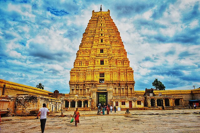 Virupaksha Temple, a majestic stone structure adorned with intricate carvings and towers against a blue sky backdrop.