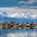 Panoramic view of the serene Dal Lake, surrounded by lush greenery and snow-capped mountains in India.