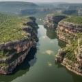 Aerial view of Gandikota, showcasing stunning red rock formations, a meandering river, and lush greenery. The landscape resembles the Grand Canyon, with rugged cliffs and a vast canyon carved by the river.